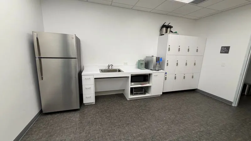 Clean office breakroom with fridge, sink and lockers